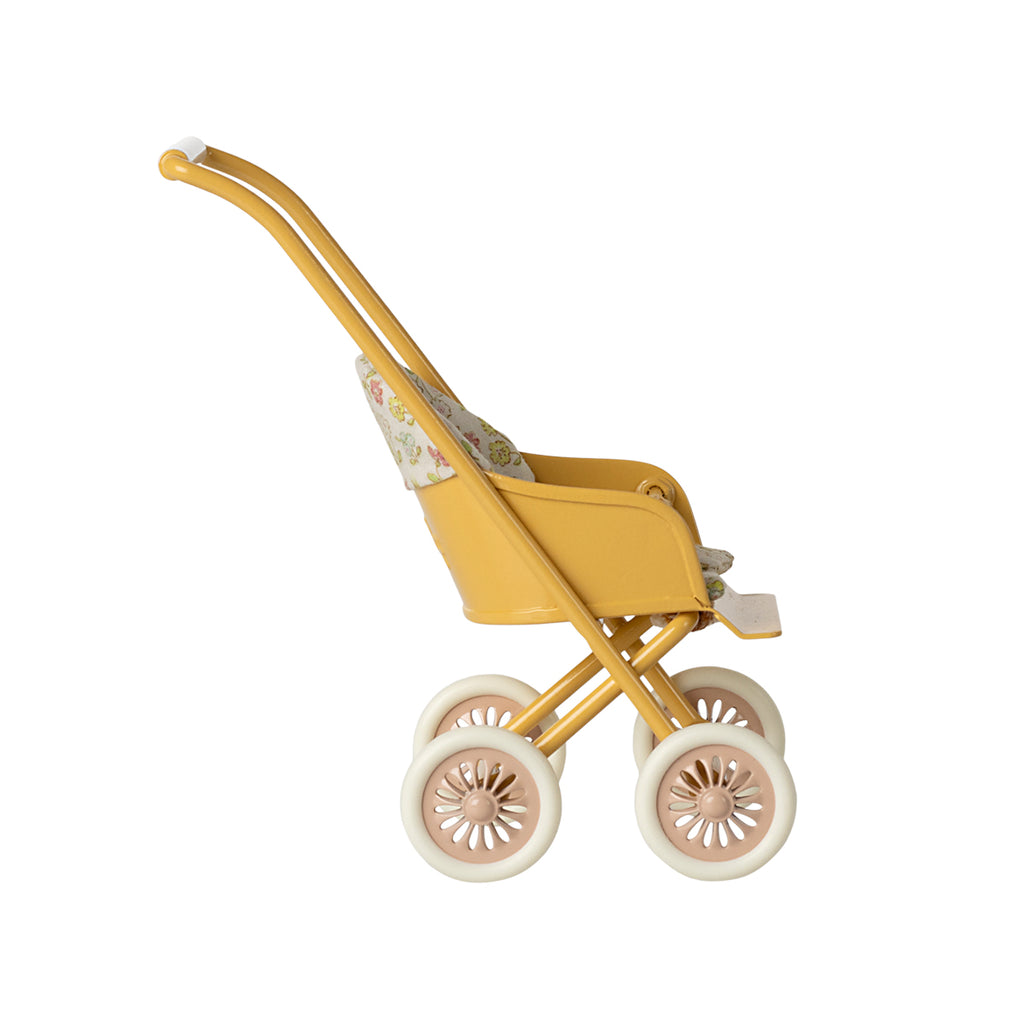 A side-facing view of the Maileg micro stroller in yellow, showcasing its vintage-inspired design with a floral seat and pink-accented wheels.