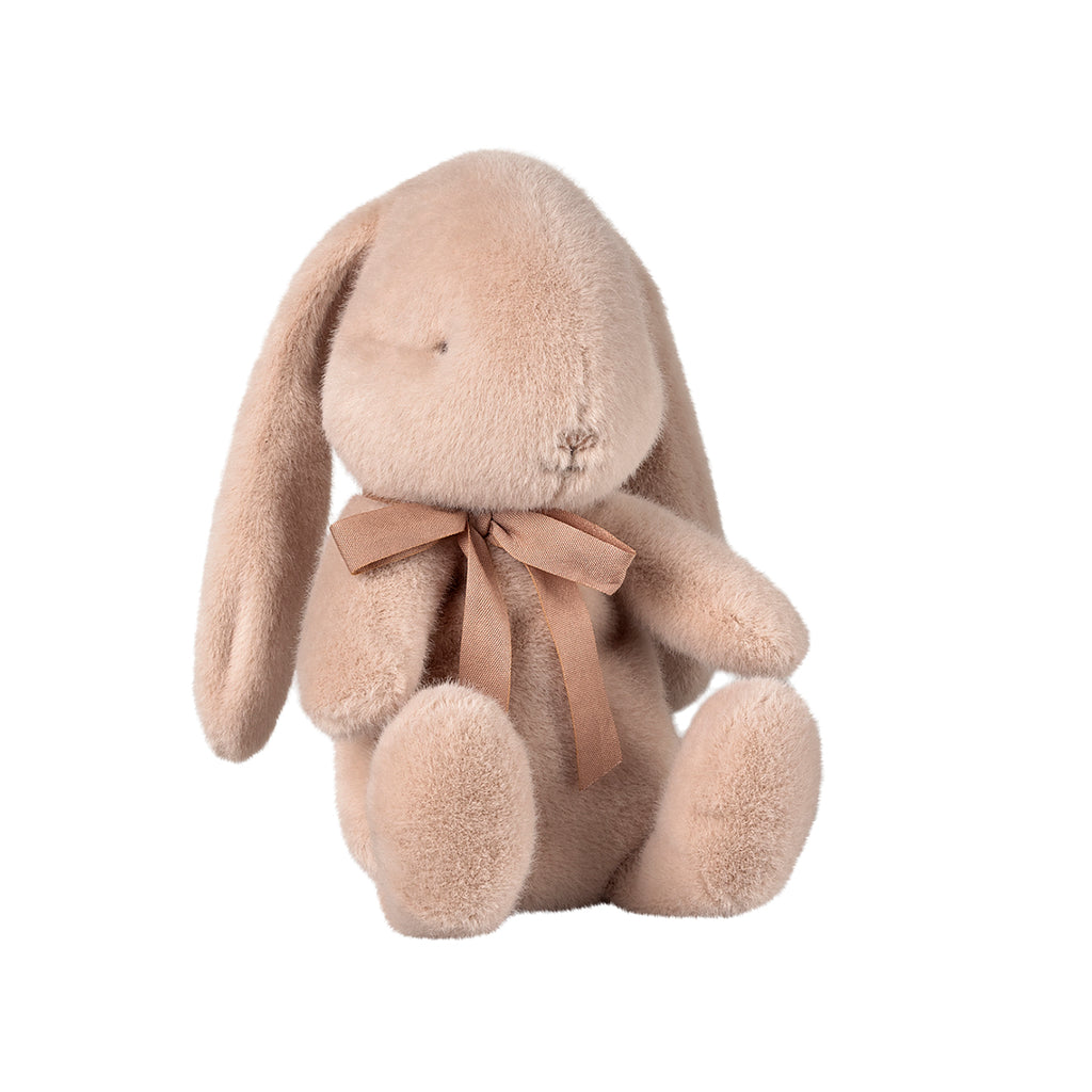 A delightful Maileg small bunny plush in a soft light powder colour, sitting sweetly with a pink bow tied around its neck.