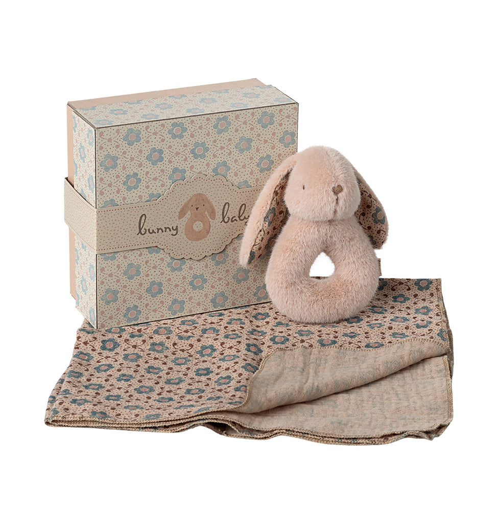 Powder Maileg rabbit rattle resting on a patterned cotton cloth, displayed next to its gift box