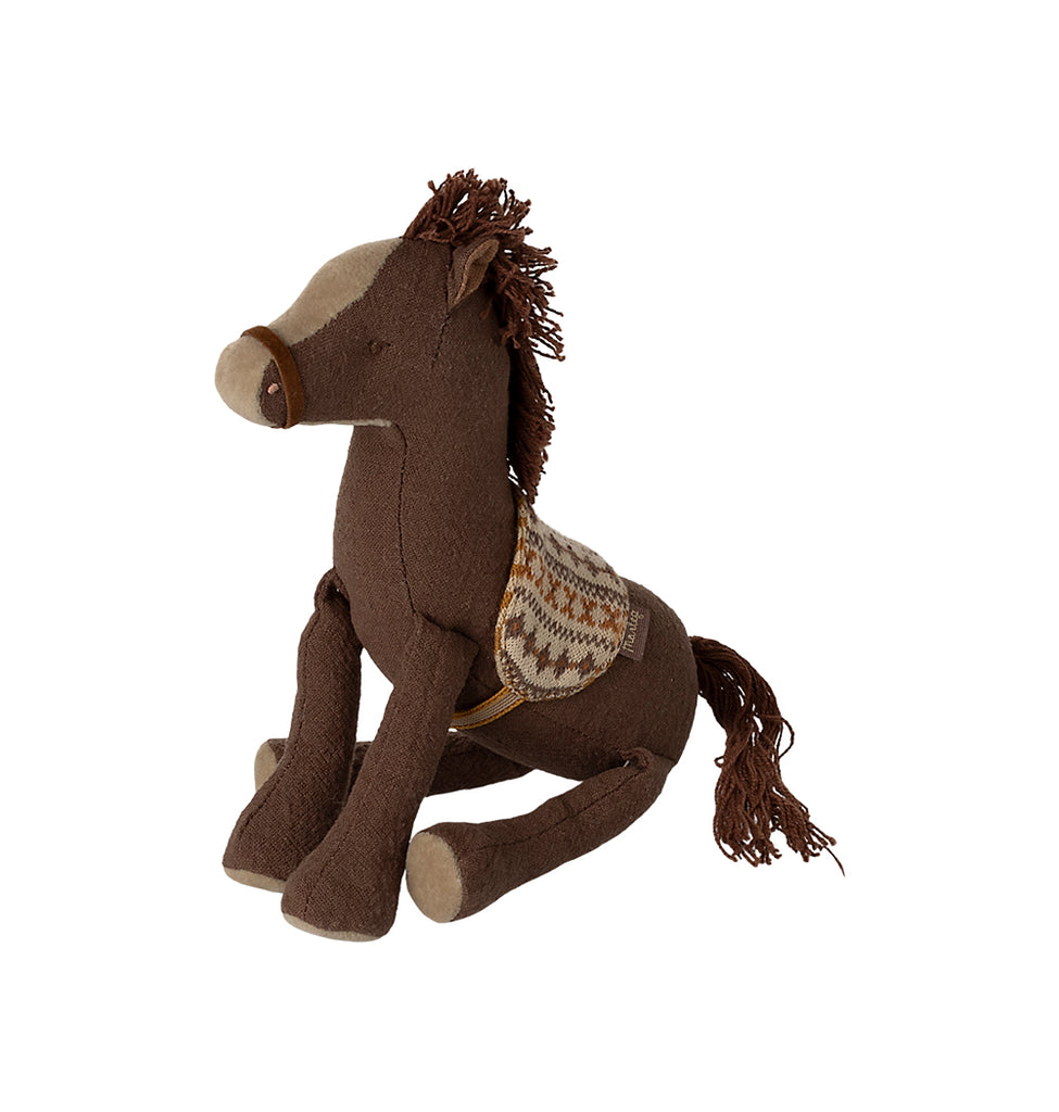 Maileg small brown pony sitting down with a cotton string mane and tail, wearing a knitted patterned fabric saddle