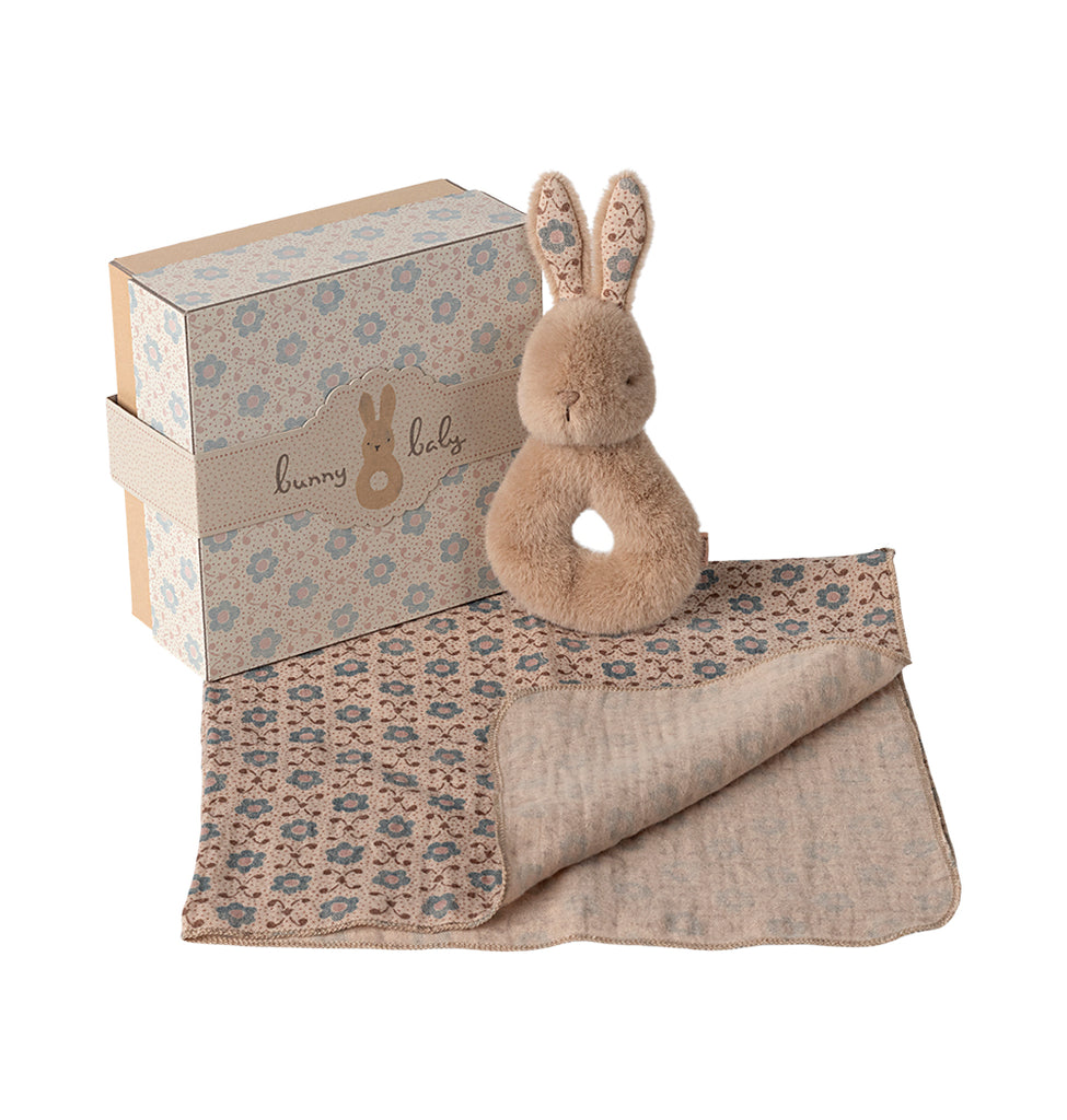 Cream Peach Maileg rabbit rattle resting on a patterned cotton cloth, displayed next to its gift box