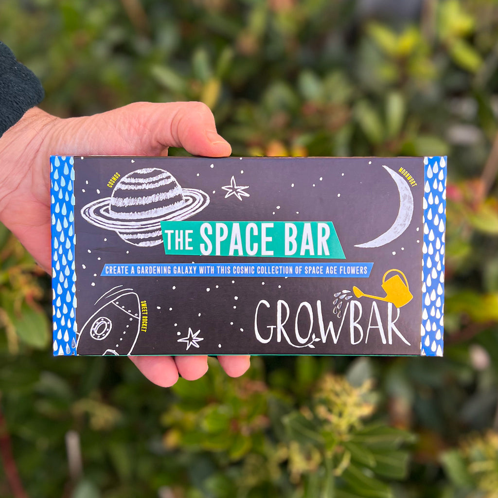 A black Growbar package labelled "The Space Bar," with cosmic illustrations of planets and stars, held against a green leafy background.