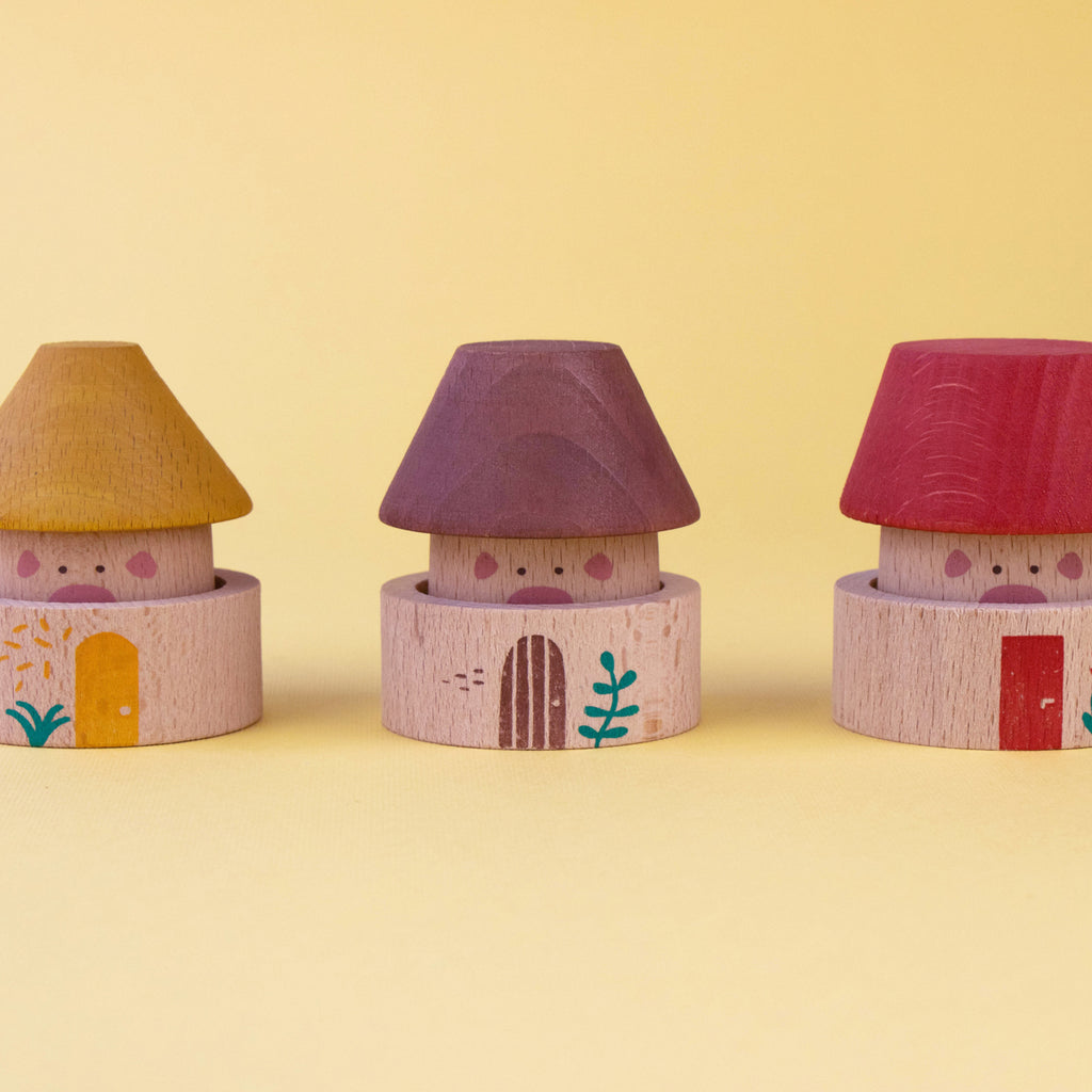 Three wooden pig houses in different colours from the Londji My Three Little Pigs game.