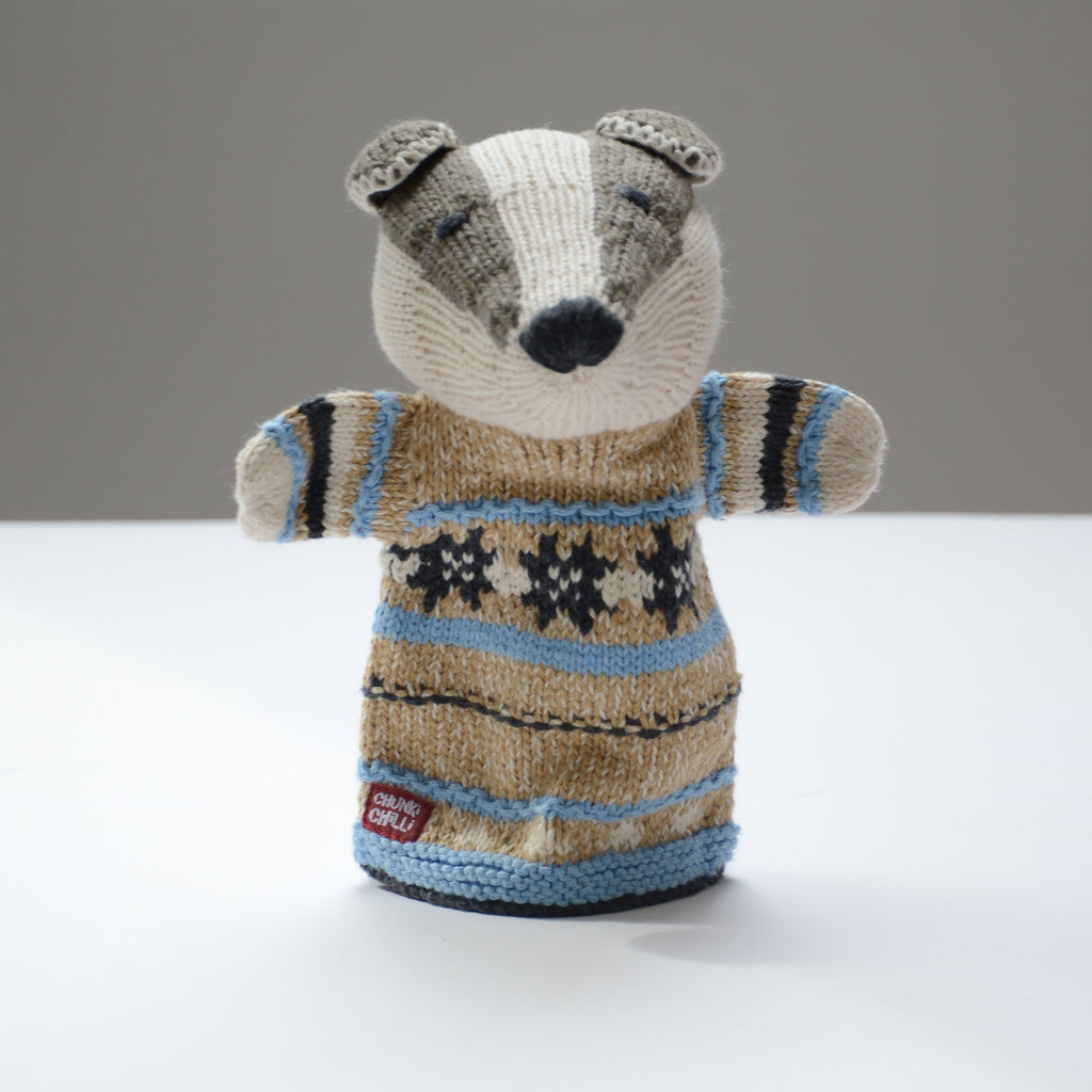 A beautifully knitted hand puppet by ChunkiChilli featuring a badger with a cosy beige, black, and blue patterned jumper, displayed on a white background.