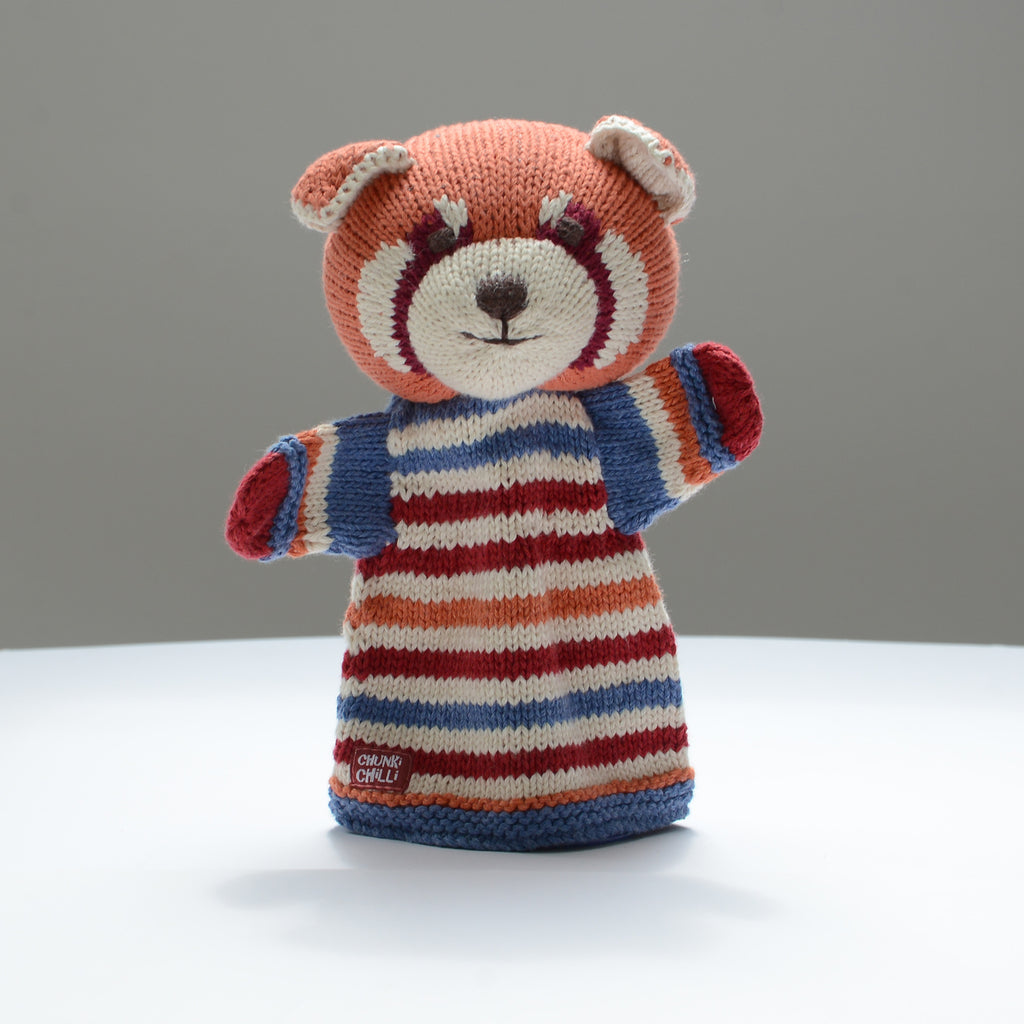 A delightful knitted hand puppet by ChunkiChilli featuring a red panda with a striped jumper in shades of red, blue, and orange, displayed on a white background.